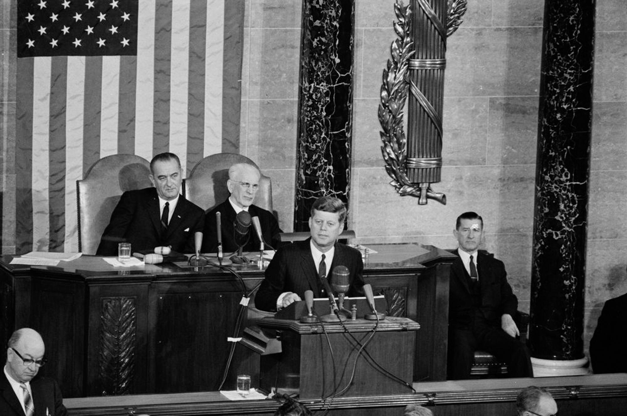 2EC3WK0 State of the Union Address, 12:33PM. President John F. Kennedy delivers his annual address to the Congress on the State of the Union in the Chamber of the House of Representatives, Capitol Building, Washington, D.C. Vice President Lyndon B. Johnson and Speaker of the House of Representatives, John W. McCormack (Massachusetts), sit at left behind the President; Clerk of the House of Representatives, Ralph R. Roberts, sits at right.