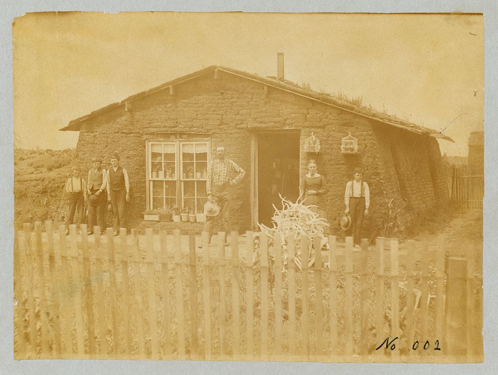 A black-and-white photograph of a homesteading family standing in front of their sod house on the Nebraska plains.