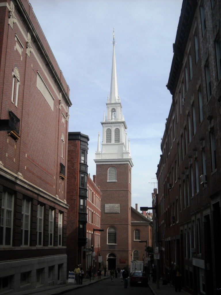 Exterior view of the Old North Church (Christ Church) in Boston’s North End, a tall brick colonial church with a white steeple against a blue sky, surrounded by historic buildings