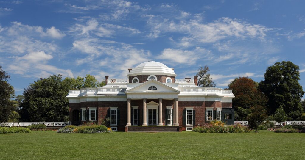 The west facade of Monticello, Thomas Jefferson’s mountaintop home in Charlottesville, Virginia, showing the iconic neoclassical dome and symmetrical architecture reflected in a pool on a clear day