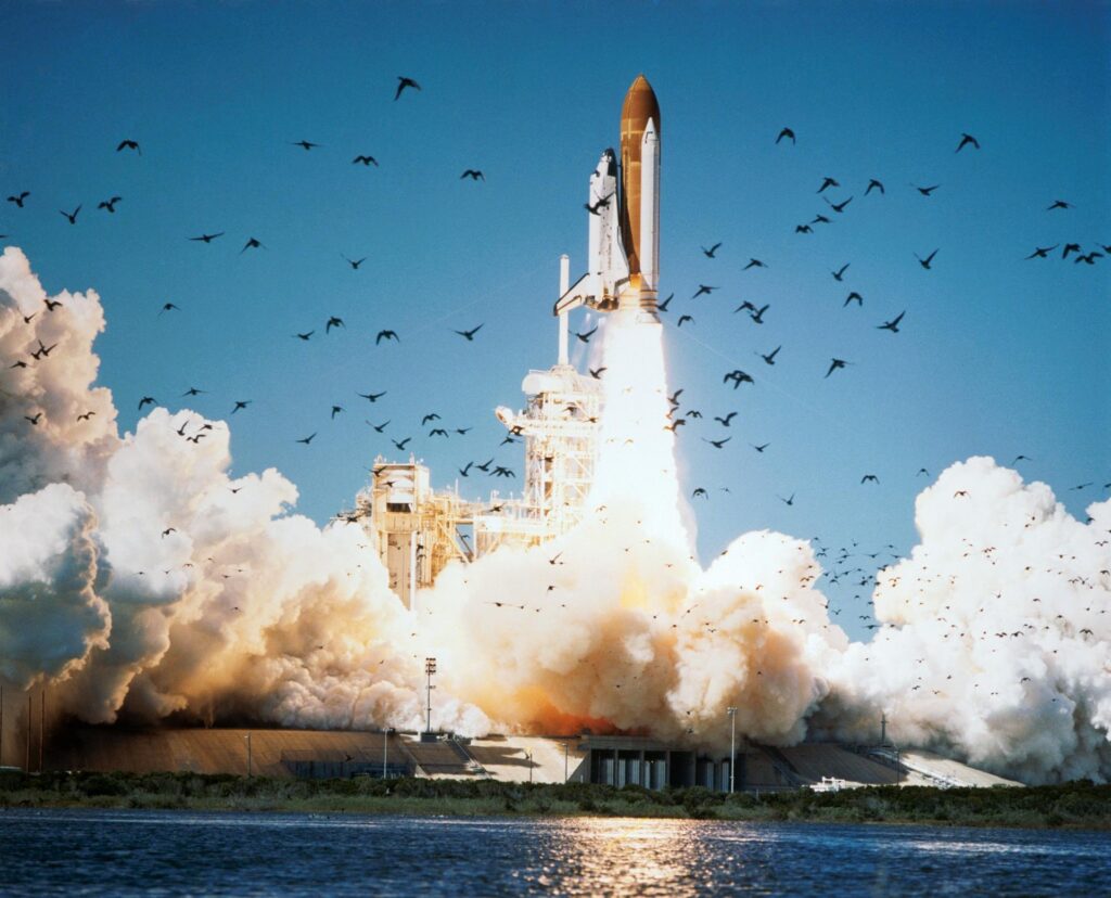 Space Shuttle Challenger launches from Pad 39B at Kennedy Space Center, rising on a column of flame and white smoke against a clear blue sky on January 28, 1986.