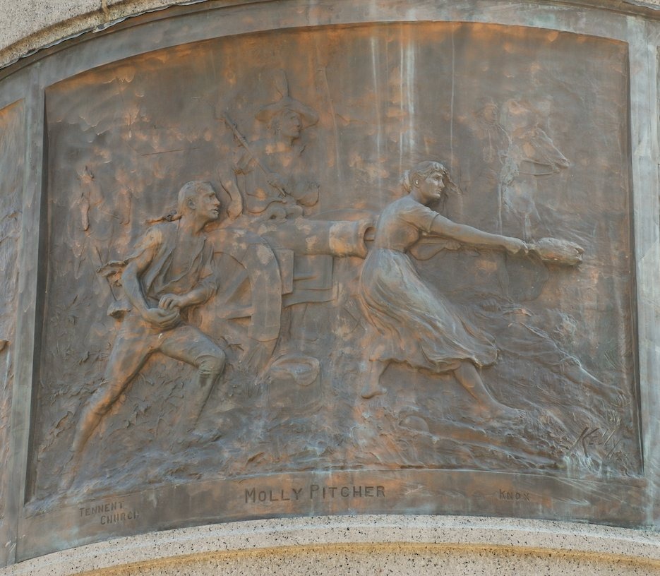 Statue and memorial monument honoring Molly Pitcher in Carlisle, Pennsylvania, featuring a bronze figure of a Revolutionary War woman beside commemorative stonework.