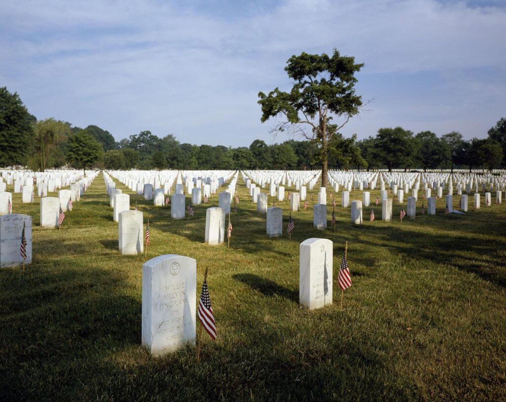 Color photograph of American flags placed beside rows of white headstones at a military cemetery during Memorial Day commemorations.