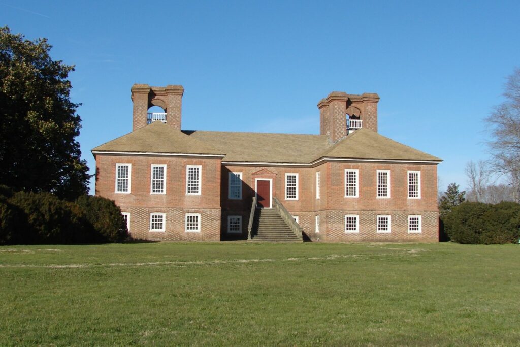 View of Stratford Hall, a large red-brick Georgian mansion overlooking the Potomac River in Virginia. The historic estate features symmetrical architecture, chimneys, and expansive lawns.