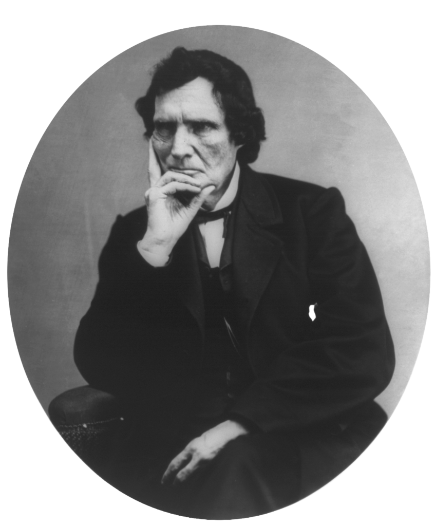 Black-and-white portrait of Congressman Thaddeus Stevens seated in a chair, wearing a dark suit, waistcoat, and bow tie, with one hand resting on a cane. He faces the camera with a serious expression.
