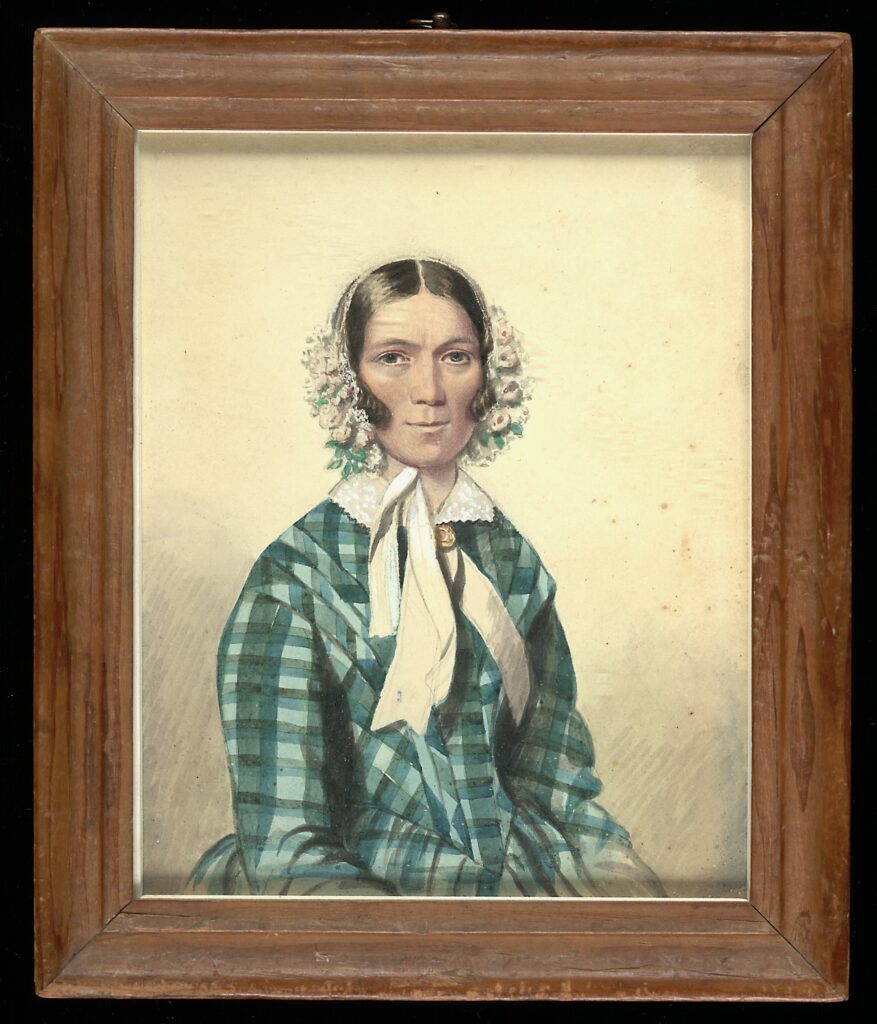 A framed watercolor portrait miniature, ca. 1840, of an unidentified woman wearing a white bonnet trimmed with pink and white flowers, a green-and-blue plaid shawl over her shoulders, a white lace collar, and a white ribbon tied in a bow at her neck, gazing directly at the viewer.